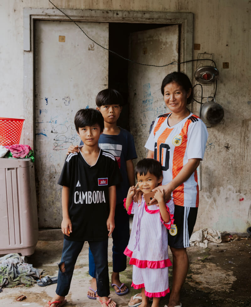 A Cambodian mother and her three children outside their home